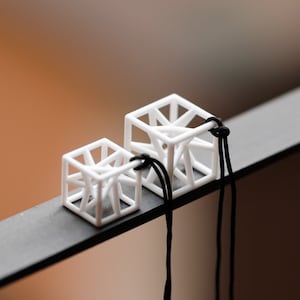 Può includere: Due collane pendenti geometriche bianche con cordini neri. Le collane sono realizzate in un design a cubo traforato stampato in 3D.