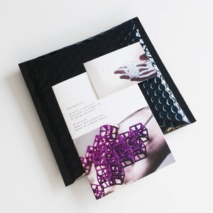 May include: A black bubble mailer with two cards. One card features a purple geometric necklace, and the other shows a similar design. Text on the card reads "3d printed jewels and accessories based on original design."