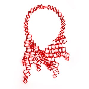Può includere: Una collana rossa fatta di cubi interconnessi. La collana ha la forma di un cerchio con una lunga coda fluida.