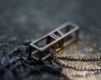 May include: A brown metal necklace with a geometric pendant. The pendant is a rectangular shape with a series of smaller squares cut out of it.