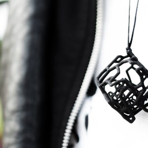 Op de afbeelding: Een zwarte ketting met een geometrische hanger gemaakt van met elkaar verbonden lijnen. De hanger is een complex, abstract ontwerp.