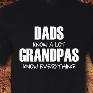 Peut inclure: T-shirt noir avec du texte blanc qui dit "Les papas en savent beaucoup Les grands-pères savent tout".