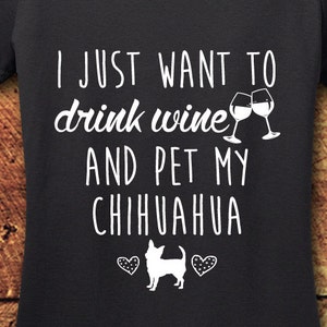 May include: A dark gray t-shirt with the text "I just want to drink wine and pet my chihuahua" in white. Two wine glasses clinking are above the text. A chihuahua silhouette is below the text with two hearts on either side.