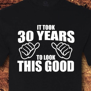 May include: Black t-shirt with white text that reads "It took 30 years to look this good". The text is surrounded by two white thumbs up symbols.