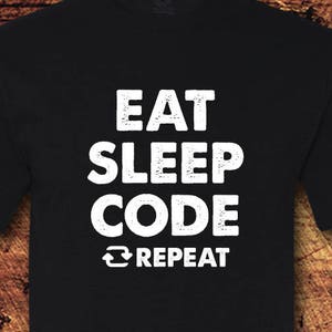 Op de afbeelding: Zwart T-shirt met witte tekst die "Eat Sleep Code Repeat" zegt.