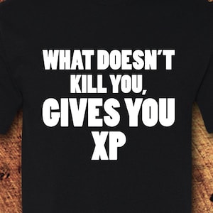 May include: Black t-shirt with the white text "WHAT DOESN'T KILL YOU, GIVES YOU XP". The shirt has short sleeves and a crew neck. The MaTees Shirt Company logo is visible in the lower right corner.