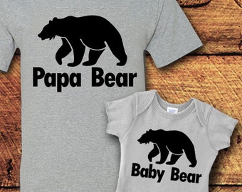 May include: A gray t-shirt with a black bear silhouette and the text "Papa Bear" and a gray baby onesie with a black bear silhouette and the text "Baby Bear".