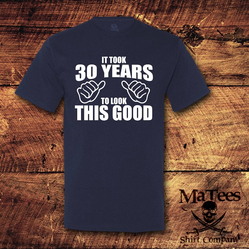 May include: A navy blue t-shirt with white text that reads "It took 30 years to look this good". The text is surrounded by two white thumbs up symbols.