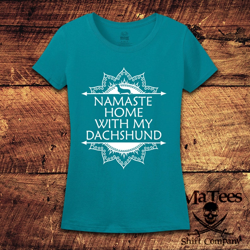 Op de afbeelding: Turquoiseblauw T-shirt met een wit mandala-ontwerp en de tekst "Namaste Home With My Dachshund".