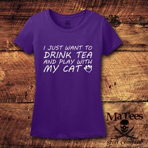 May include: Purple short-sleeved t-shirt with white text that reads "I just want to drink tea and play with my cat" with a paw print and heart graphic.