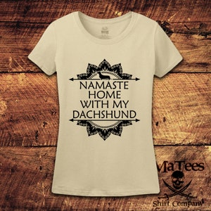 Op de afbeelding: Een beige t-shirt met een zwart mandala-ontwerp en de tekst "Namaste Home With My Dachshund".