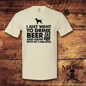 May include: A beige t-shirt with a black silhouette of a Labrador Retriever and the text "I just want to drink beer and hang with my Labrador".
