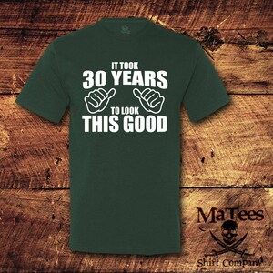 May include: A dark green t-shirt with white text that reads "It took 30 years to look this good". The text is surrounded by two thumbs up symbols.