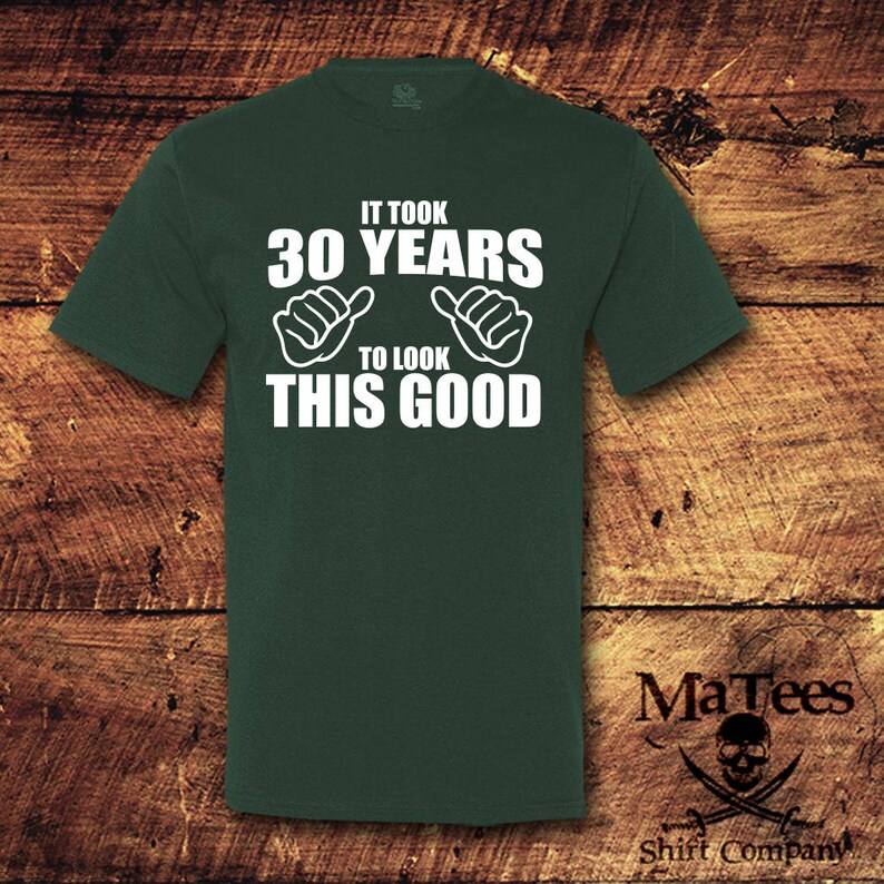 May include: A dark green t-shirt with white text that reads "It took 30 years to look this good". The text is surrounded by two thumbs up symbols.