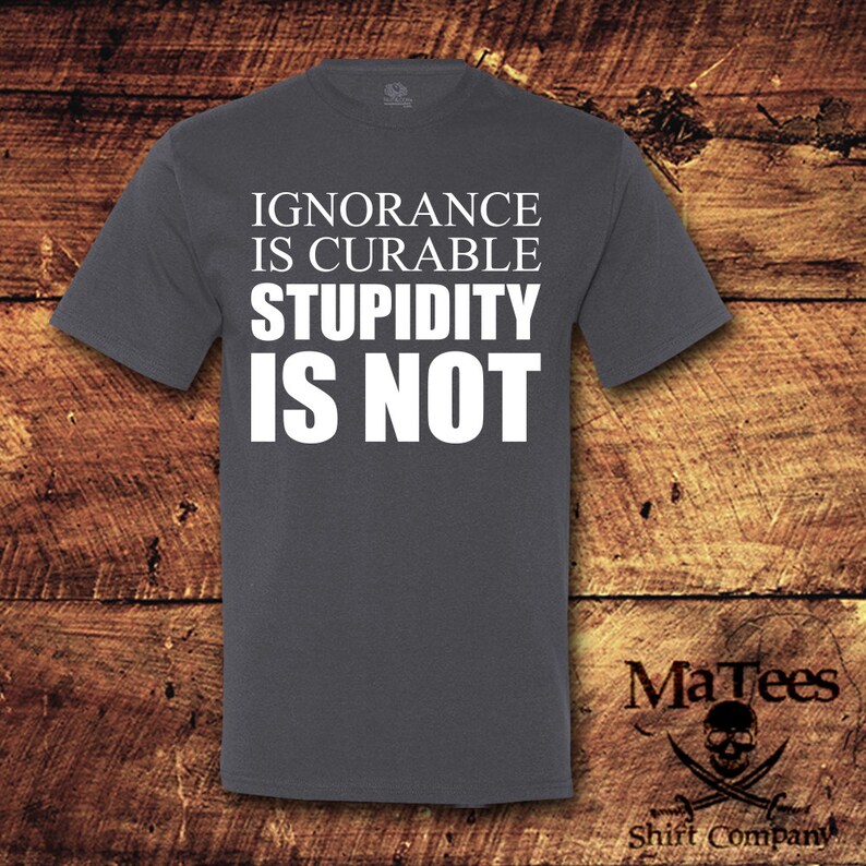 May include: A dark gray t-shirt with the text "IGNORANCE IS CURABLE STUPIDITY IS NOT" printed in white.