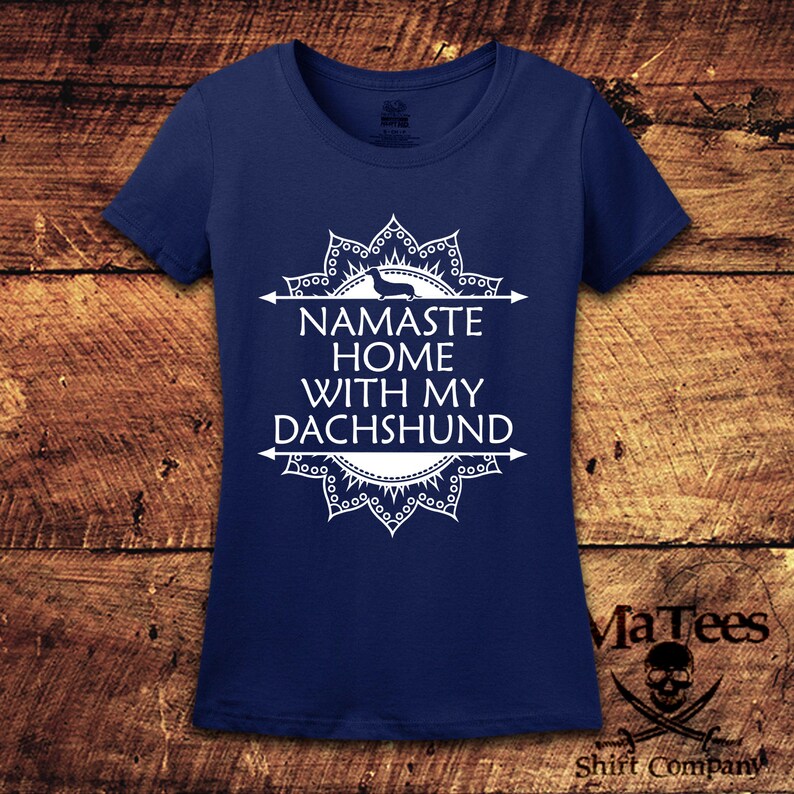 Op de afbeelding: Een marineblauw t-shirt met een wit mandala-ontwerp en de tekst "Namaste Home With My Dachshund".