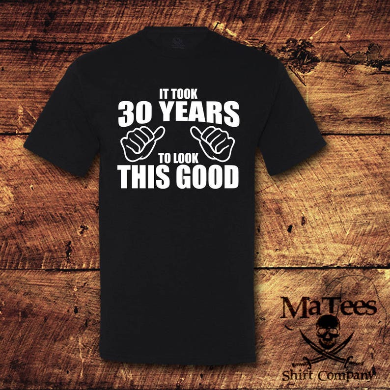May include: Black t-shirt with white text that reads "It took 30 years to look this good". The text is surrounded by two white thumbs up symbols.