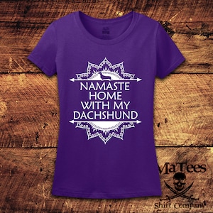 Op de afbeelding: Paars T-shirt met een wit mandala-ontwerp en de tekst "Namaste Home With My Dachshund".