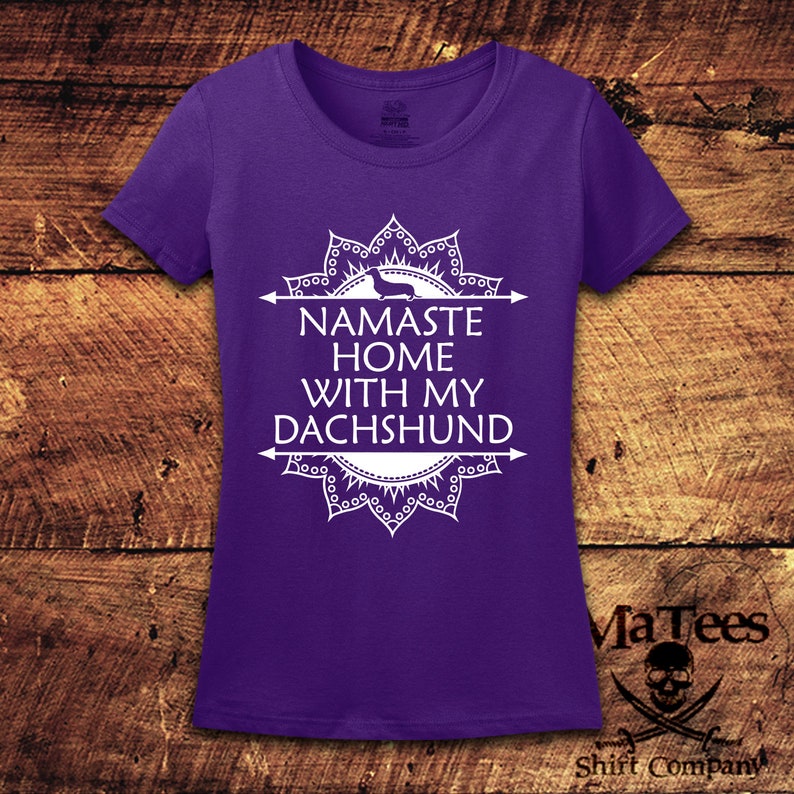 Op de afbeelding: Paars T-shirt met een wit mandala-ontwerp en de tekst "Namaste Home With My Dachshund".