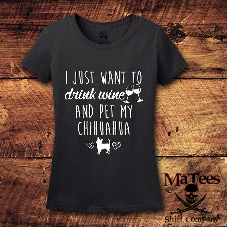 May include: A dark gray t-shirt with the text "I just want to drink wine and pet my chihuahua" in white. Two wine glasses clinking are above the text. A chihuahua silhouette is below the text with two hearts on either side.