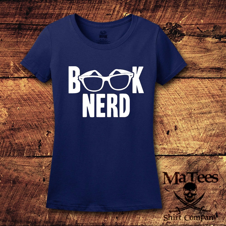 May include: Navy blue t-shirt with the white text "BOOK NERD" and glasses graphic. The shirt is made of a soft material and is perfect for book lovers. The shirt has a crew neck and short sleeves.