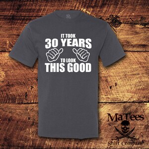 May include: A dark gray t-shirt with white text that reads "It took 30 years to look this good". The text is surrounded by two thumbs up hand gestures.