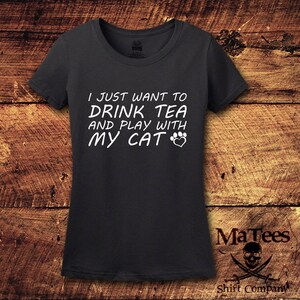 May include: A dark gray t-shirt with the text "I just want to drink tea and play with my cat" in white lettering with a paw print and heart graphic.