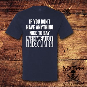 May include: Navy blue t-shirt with the text "IF YOU DON'T HAVE ANYTHING NICE TO SAY WE HAVE A LOT IN COMMON" in white. The shirt also features the MaTees logo and "Shift Company" text.