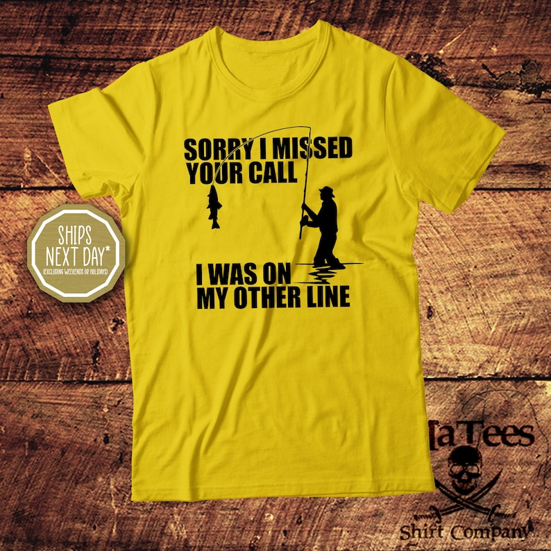 May include: Yellow t-shirt with black text and a fishing-themed graphic. The text reads "Sorry I missed your call, I was on my other line." A silhouette of a fisherman and a fish are also featured.