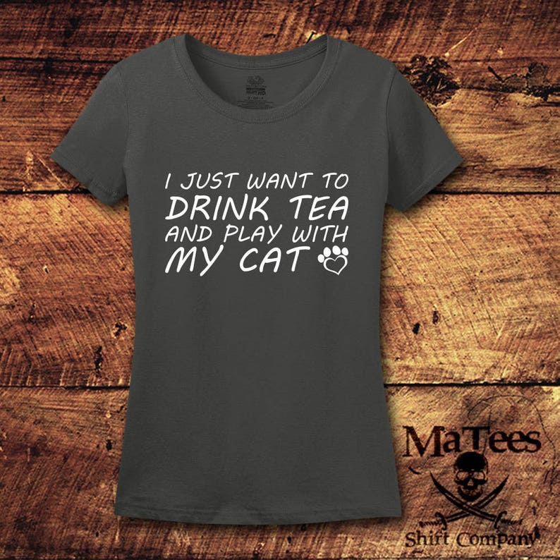 May include: A dark gray t-shirt with the text "I just want to drink tea and play with my cat" in white lettering. A paw print and heart are included in the text.