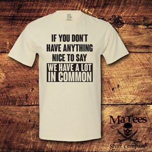 May include: Cream-colored t-shirt with the text "IF YOU DON'T HAVE ANYTHING NICE TO SAY WE HAVE A LOT IN COMMON" in black. The shirt also features the "MaTees" logo with a skull and crossbones.