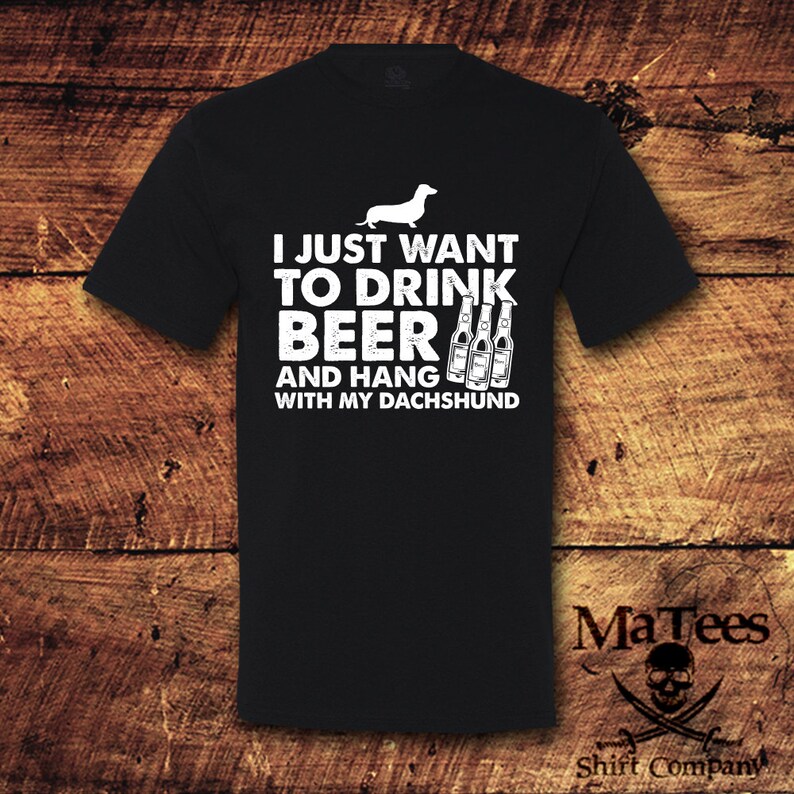 May include: Black t-shirt with white text that reads "I just want to drink beer and hang with my dachshund". The shirt also features a white silhouette of a dachshund and three bottles of beer.