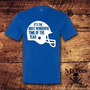 May include: Royal blue t-shirt with white text that reads "It's the most wonderful time of the year" and a white football helmet graphic.