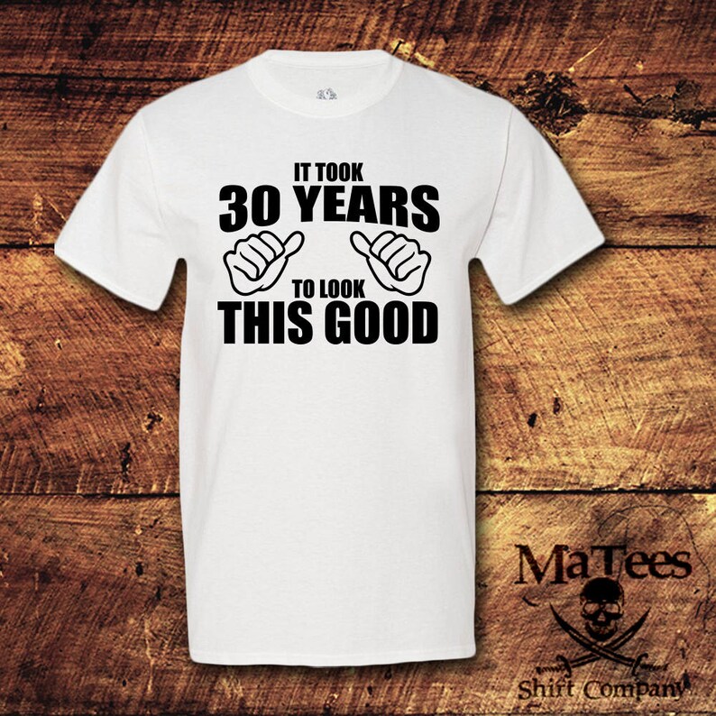 May include: White t-shirt with black text that reads "It took 30 years to look this good". The text is surrounded by two black hand gestures with thumbs up.