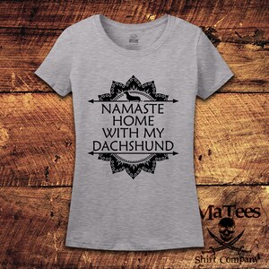 Op de afbeelding: Grijs T-shirt met een zwart mandala-ontwerp en de tekst "Namaste Home With My Dachshund".