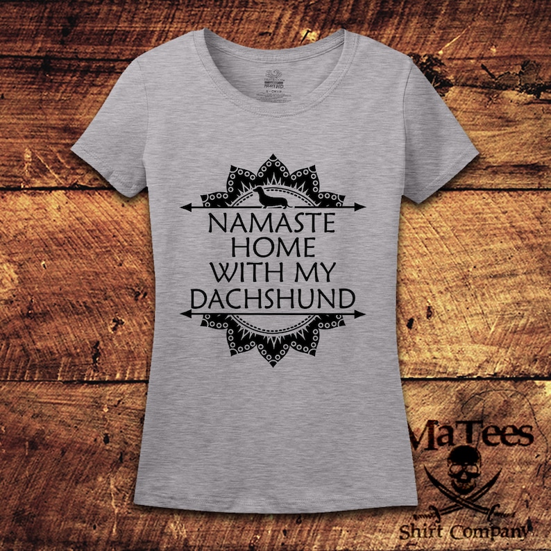 Op de afbeelding: Grijs T-shirt met een zwart mandala-ontwerp en de tekst "Namaste Home With My Dachshund".