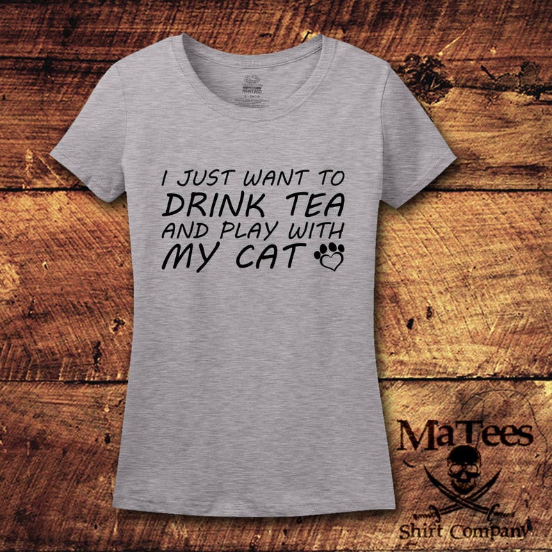 May include: Gray t-shirt with the text "I just want to drink tea and play with my cat" in black lettering. A paw print and heart are included in the text.