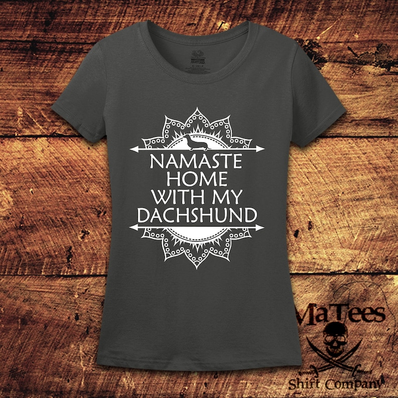 Op de afbeelding: Een donkergrijs T-shirt met een wit mandala-ontwerp en de tekst "Namaste Home With My Dachshund".