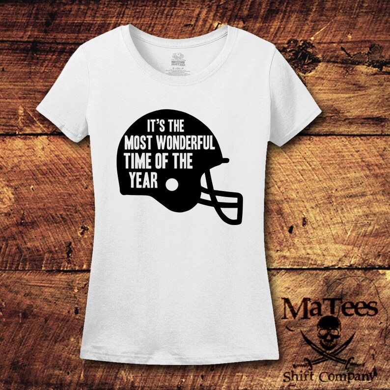 K&ouml;nnte beinhalten: Wei&szlig;es T-Shirt mit schwarzem Text, der "Es ist die sch&ouml;nste Zeit des Jahres" lautet, und einer schwarzen Footballhelm-Grafik.