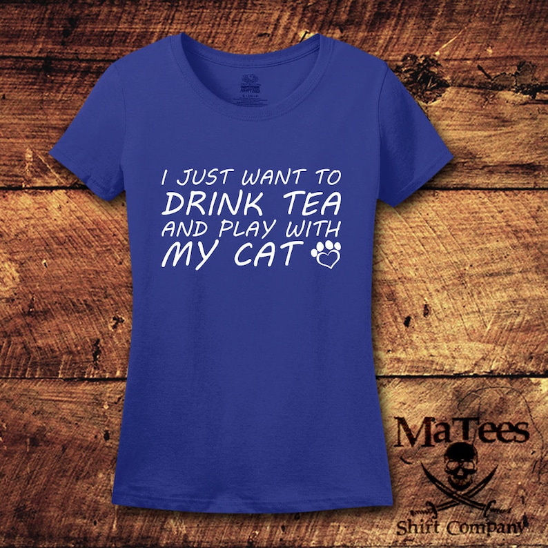 May include: A royal blue t-shirt with white text that reads "I just want to drink tea and play with my cat" with a paw print and heart symbol.