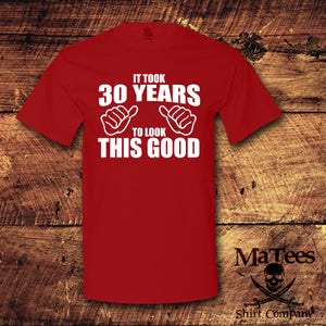 May include: Red t-shirt with white text that reads "It took 30 years to look this good". The text is surrounded by two white hand gestures with thumbs up.