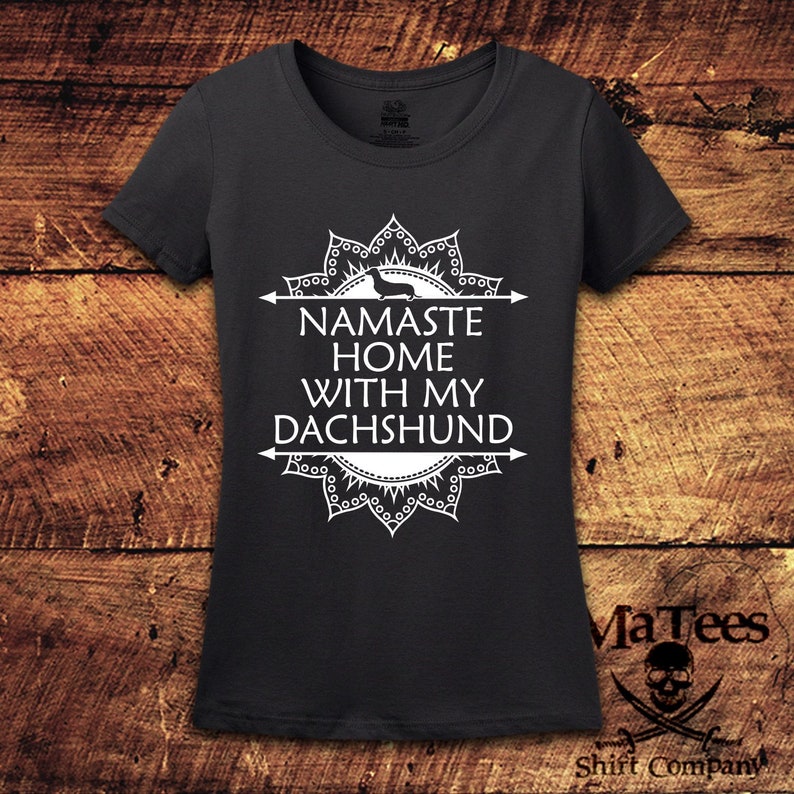 Op de afbeelding: Een donkergrijs T-shirt met een wit mandala-ontwerp en de tekst "Namaste Home With My Dachshund".