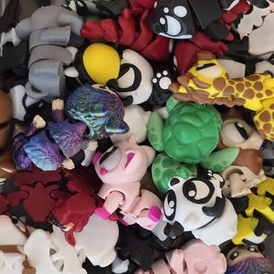 May include: A selection of colourful, articulated animal figurines. The assortment includes turtles, pandas, giraffes, and other creatures in various colours like green, pink, yellow, and black. The toys appear to be 3D-printed.