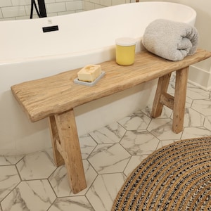May include: A rustic wooden bench with a natural finish, holding a gray towel, a yellow container, and a bar of soap on a gray soap dish. The bench is positioned near a white bathtub.