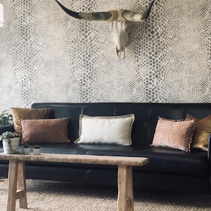 May include: A black leather sofa with decorative pillows in shades of brown and pink. A wooden bench sits in front of the sofa, and a cow skull hangs on the patterned wall behind it. The room is decorated in a rustic style.