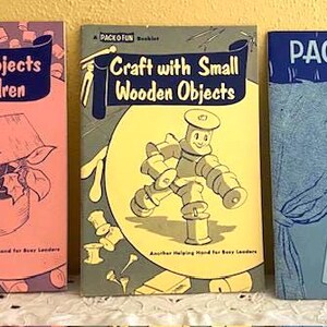 May include: Three vintage Pack-O-Fun booklets. The titles are "Tin Can Projects for Children", "Craft with Small Wooden Objects", and "Skit Book No. 1". The covers feature illustrations in pink, yellow, and blue, with text in dark blue.