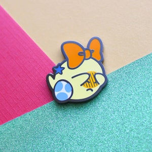 Pode incluir: Um personagem de desenho animado amarelo com uma estrela azul e um olho azul e branco, usando um grande la&ccedil;o laranja. O personagem est&aacute; olhando para baixo e tem uma express&atilde;o triste.