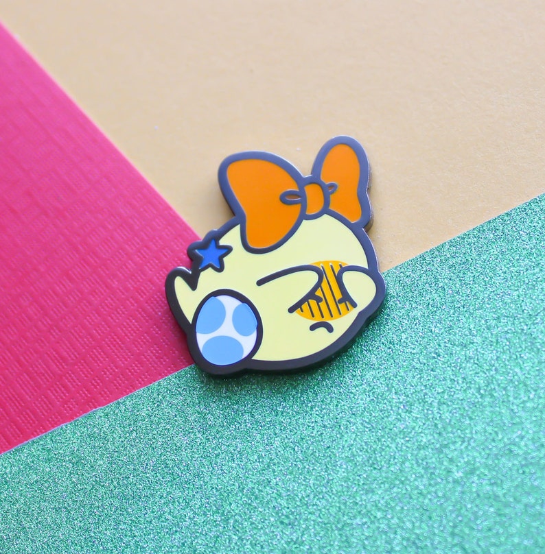 Pode incluir: Um personagem de desenho animado amarelo com uma estrela azul e um olho azul e branco, usando um grande la&ccedil;o laranja. O personagem est&aacute; olhando para baixo e tem uma express&atilde;o triste.