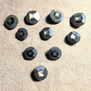 May include: A collection of ten circular buttons featuring a dark grey metallic finish with a faceted, pyramid-shaped centre. Each button displays a reflective, light-catching surface that creates a distinct contrast between the dark edges and the centre.