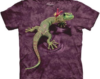 Może przedstawiać: Fioletowy t-shirt z nadrukiem zielonego gekona na przodzie. Gekon ma czerwony i różowy kwiat na głowie.